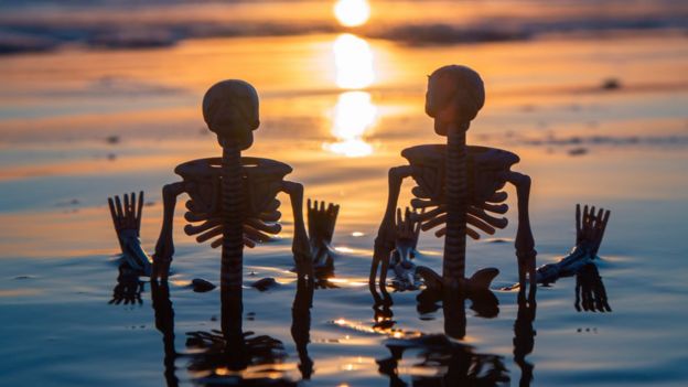 Dos esqueletos sentados en la playa.